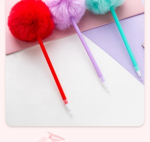 Close-up of colorful ballpoint pens with decorative plush pom-poms on a pastel geometric background