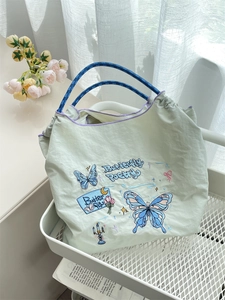 Detail of embroidered butterfly pattern and woven rope handle on green tote bag