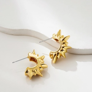Macro detail of 18K gold sunburst C-shape earrings on white stone background