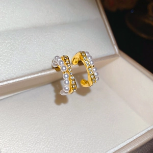 Close-up of C-shaped gold hoop earrings with white pearls and sparkling rhinestones