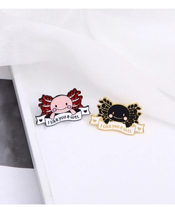 Detail of pink and black axolotl pins with I like you a lotl text on a soft white fabric