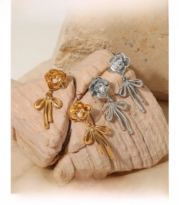 Detail of flower and bow earrings with pearls and rhinestones on beige stone