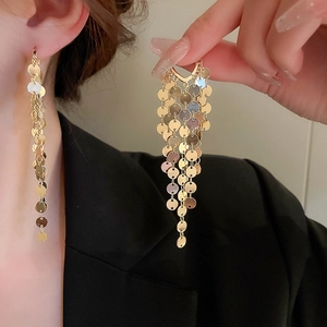 Close-up of long layered gold sequin fringe earrings with a dynamic metallic tassel drop