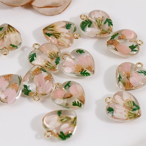 Macro detail of heart resin charms with pink dried flowers and leaves for jewelry DIY