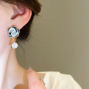 Detail of French enamel camellia drop earrings with blue petals and white pearl on model