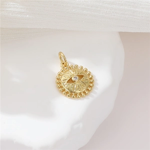Close-up of a gold round sun and moon pendant with an evil eye zircon inlay on white fabric