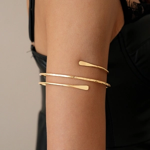 Detailed view of golden spiral arm cuff with hammered texture on a model's arm