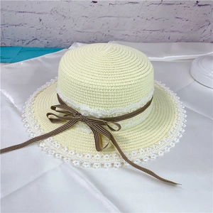 Detail of flat top straw hat featuring delicate white lace trim and plaid ribbon bow