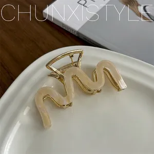 Detail of wavy gold metal hair claw with cream acetate inlay on white ceramic plate