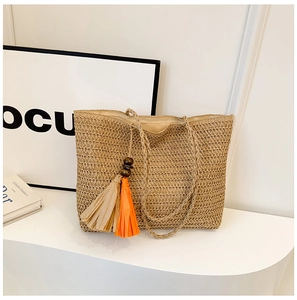 Detail of hand-woven straw tote bag featuring colorful orange and beige tassel charms