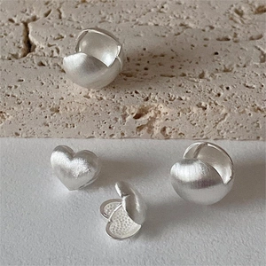 Detailed view of matte brushed silver heart earrings on a minimalist stone background