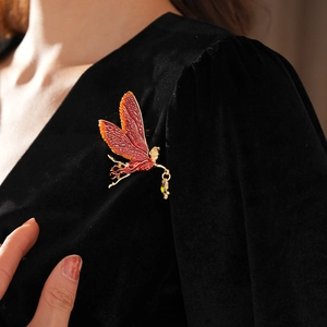Detail of vintage enamel fairy brooch with orange wings on black velvet fabric