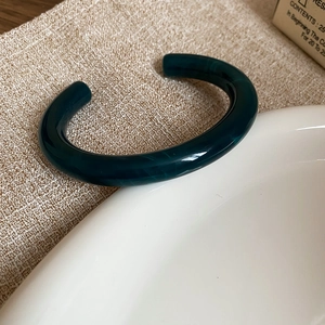 Macro detail of dark green marble textured resin cuff bracelet on white ceramic plate