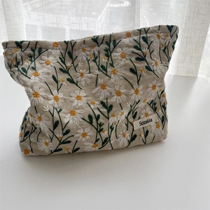 Detailed embroidery of white daisy petals and yellow stamens on a beige fabric cosmetic bag
