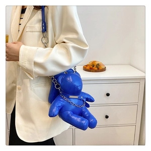 Detail of blue teddy bear PU leather bag with chain on a model in a white suit