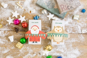 Christmas gift box with festive socks featuring Santa and owl designs on snowy wood