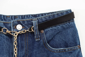 Dettaglio vita in denim blu scuro con cintura in pelle nera e catena in metallo dorato