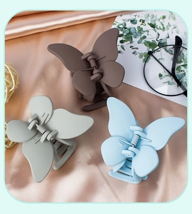 Detailed shot of three matte butterfly hair claws in brown, grey, and blue on silk