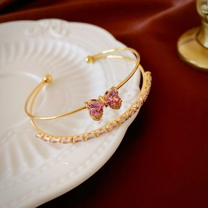 Detail of gold zircon bow bracelet and rectangular crystal chain on white relief plate