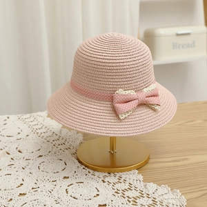 Close-up of pink straw sun hat with polka dot ribbon and lace bow on a metal stand