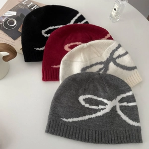 Detailed view of four knitted beanies in black, red, cream, and grey with bow patterns