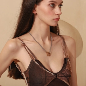 Detail of silver chain necklace with gold ring pendant worn by a model in soft light