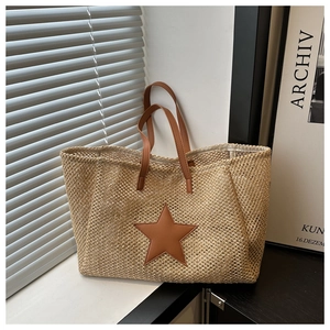 Detail of woven straw tote bag featuring a brown star leather patch and dual handles
