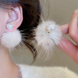 Close-up of elegant white pearl and plush fur ball earrings on a female model