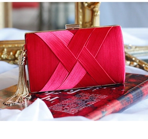 Macro view of red satin clutch bag featuring gold tassel fringe and luxury metallic clasp
