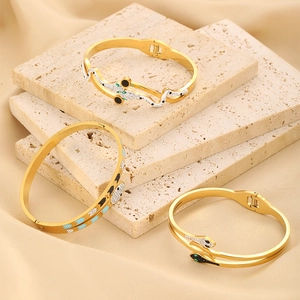 Detailed view of three gold snake-shaped bangles with colorful gemstones on marble slabs