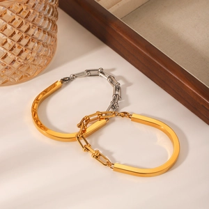 Détail de bracelets à maillons en U dorés et bicolores sur un plateau en bois chic