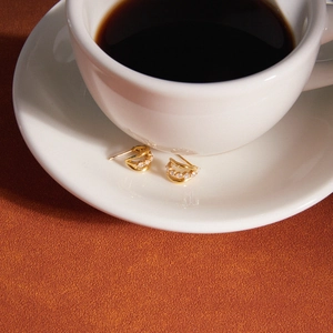 Detailed view of gold C-shaped earrings with cubic zirconia on a white ceramic saucer