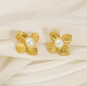 Detail of gold flower earrings with brushed metal texture and central pearl accent