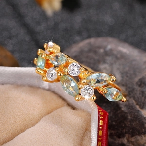 Macro detail of leaf-shaped gold ring with blue stones on a velvet jewelry box
