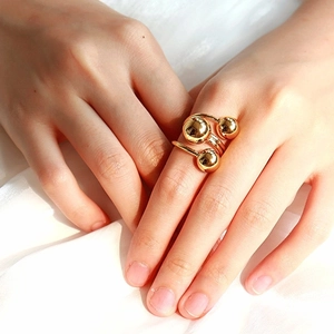Detailed close-up of adjustable gold triple ball ring on finger with glossy finish
