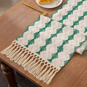 Detail of green and beige woven cotton linen table runner with boho tassels on wood table