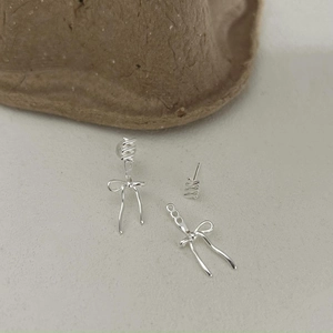 Detail shot of silver bow drop earrings and spiral studs set on a textured surface
