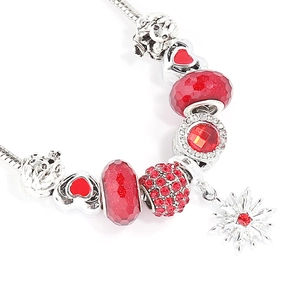 Detailed view of red charms and a snowflake pendant on a silver snake chain bracelet