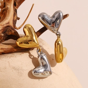 Polished two-tone heart stud earrings in 18K gold and silver finish on a branch