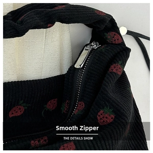 Detail of silver metal zipper and strawberry embroidery on black corduroy bag surface
