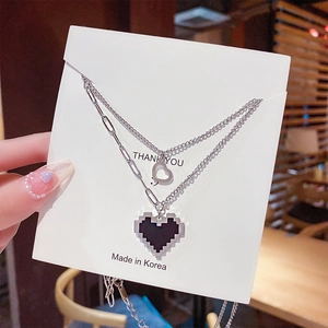 Détail de colliers argentés superposés avec cœurs ajourés et pendentifs pixel noirs
