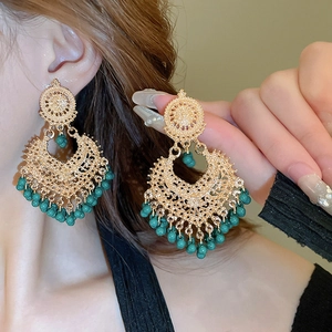 Detailed view of hollow vintage gold tassel earrings with green beads on a model
