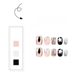 Close-up of pink and black short press-on nails with spider, star, and text patterns