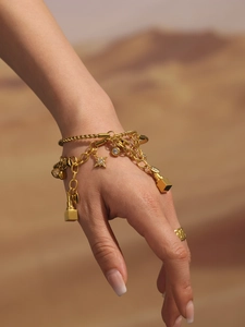 Makroansicht des goldenen Bettelarmbands mit Sternen-Anhängern am Handgelenk im Wüstensand