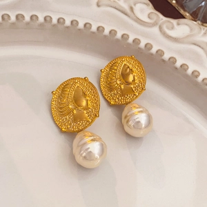 Detail of vintage gold coin earrings with irregular white pearls on ceramic tray