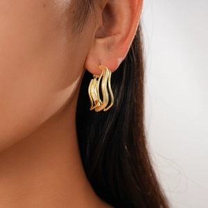 Close-up of gold layered wavy hoop earrings with a matte texture on model's ear