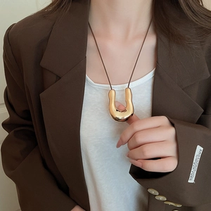 Ciondolo a forma di U in metallo dorato su cordino di cuoio indossato su blazer