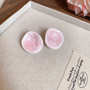 Detail of pink resin earrings with silver edges and shell-like texture on beige tray