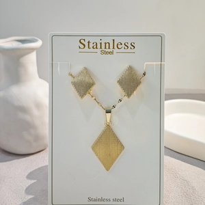 Detail of textured geometric rhombus necklace and earrings set in golden stainless steel