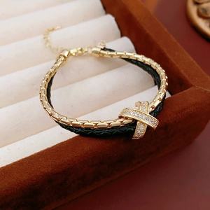Detail of gold-plated bracelet with double-layer cross charm and black leather texture